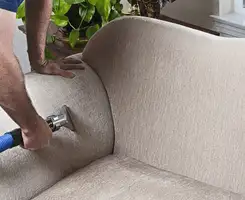 Professional upholstery cleaner deep-cleaning a fabric sofa with a handheld extraction tool and hose in Denver, CO.